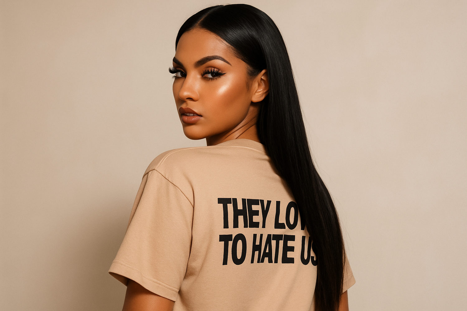 "A beautiful mixed girl with features similar to Kim Kardashian. She has glowing nude-toned skin, long sleek dark hair, contoured makeup, full lips, and bold lashes. She's wearing an oversized nude t-shirt with the words 'They Love to Hate Us' written on the back. She is turning her head over her shoulder, giving a confident and fierce 'baddie' expression. The background is minimal and aesthetic, focusing on her attitude and style."

